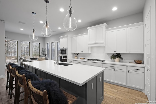 kitchen featuring white cabinetry, decorative light fixtures, stainless steel appliances, and an island with sink