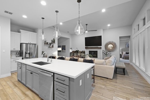 kitchen with sink, a kitchen island with sink, hanging light fixtures, stainless steel appliances, and white cabinets