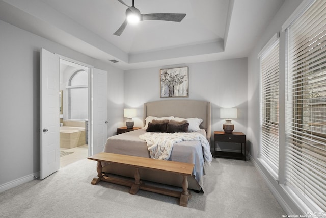 bedroom with ceiling fan, ensuite bath, a raised ceiling, and light carpet