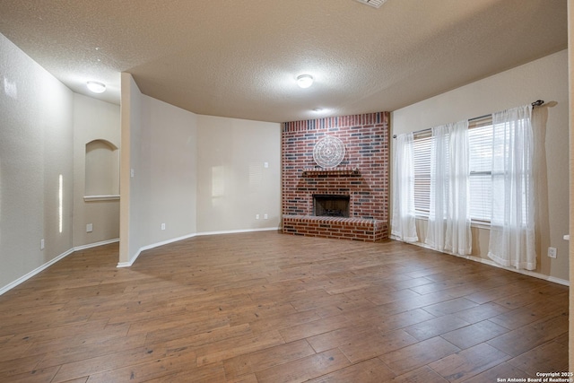 unfurnished living room featuring a brick fireplace, a textured ceiling, baseboards, and wood finished floors