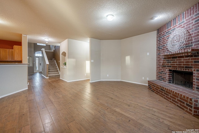 unfurnished living room featuring a brick fireplace, a textured ceiling, wood finished floors, baseboards, and stairs