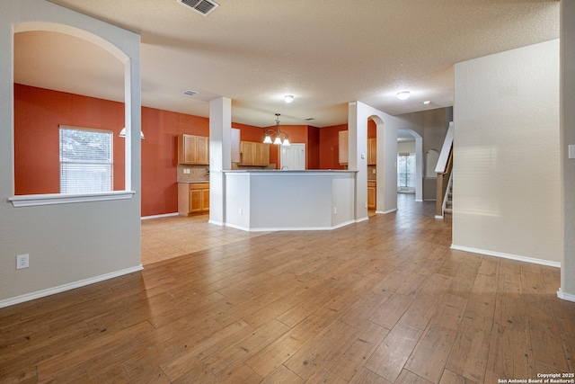 unfurnished living room with arched walkways, a healthy amount of sunlight, and light wood finished floors