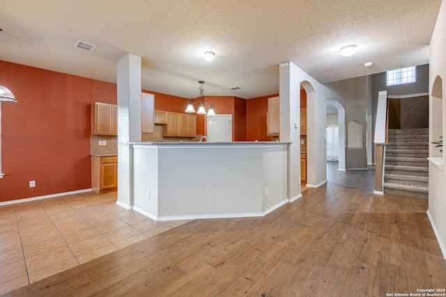 kitchen with arched walkways, hanging light fixtures, light wood-style flooring, and visible vents