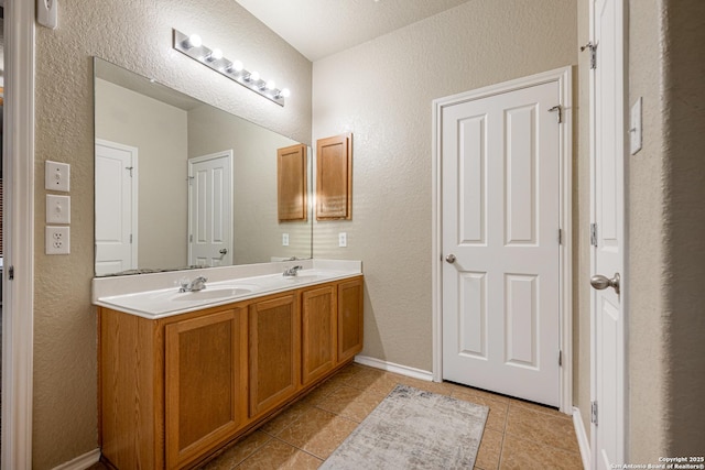 full bath featuring a textured wall, a sink, baseboards, tile patterned floors, and double vanity