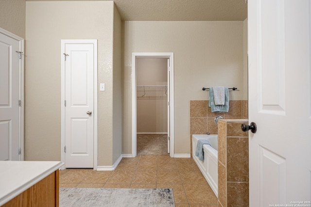 full bath featuring a walk in closet, vanity, tile patterned flooring, baseboards, and a bath