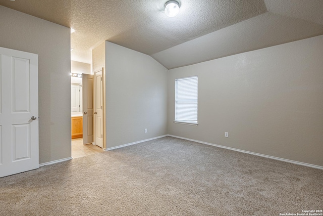 unfurnished bedroom featuring a textured ceiling, ensuite bathroom, light colored carpet, baseboards, and vaulted ceiling