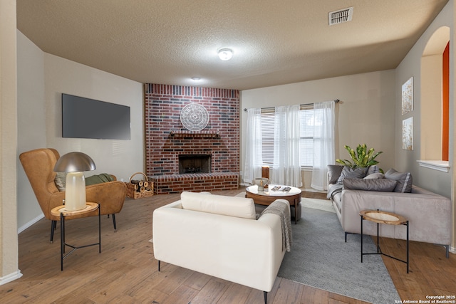 living room with visible vents, baseboards, light wood-style flooring, a textured ceiling, and a brick fireplace