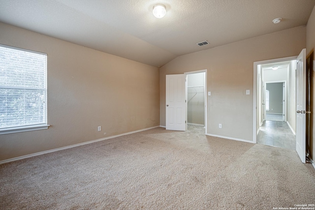 unfurnished bedroom featuring lofted ceiling, light colored carpet, visible vents, a spacious closet, and a textured ceiling