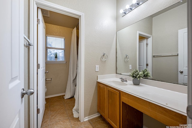 bathroom featuring baseboards, a textured wall, toilet, tile patterned flooring, and vanity