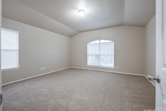 carpeted empty room with baseboards, vaulted ceiling, and a textured ceiling