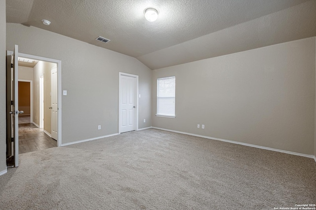 empty room with a textured ceiling, light carpet, visible vents, baseboards, and vaulted ceiling