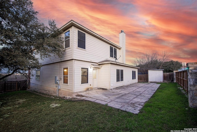 back of property at dusk featuring a patio, a fenced backyard, a storage shed, an outdoor structure, and a chimney