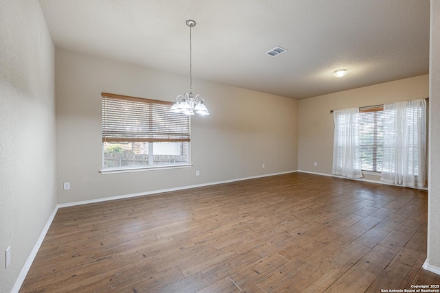 empty room featuring a healthy amount of sunlight, an inviting chandelier, visible vents, and wood finished floors