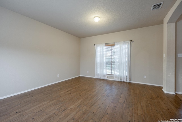 empty room featuring dark wood-style floors, baseboards, visible vents, and a textured ceiling