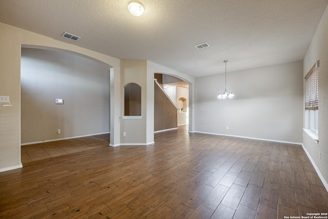 unfurnished room featuring a textured ceiling, dark wood finished floors, visible vents, and an inviting chandelier