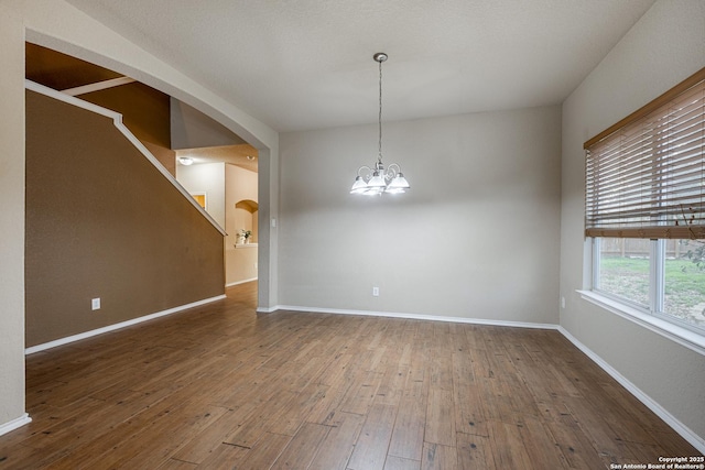 empty room with arched walkways, an inviting chandelier, baseboards, and wood finished floors