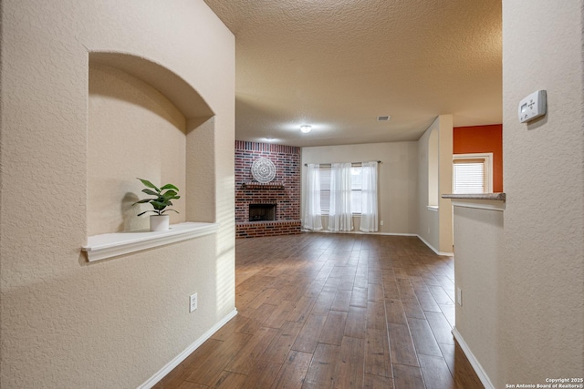 unfurnished living room featuring a brick fireplace, a textured ceiling, wood finished floors, and a textured wall