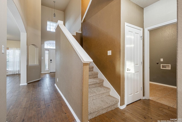 stairs featuring arched walkways, a towering ceiling, baseboards, and wood finished floors