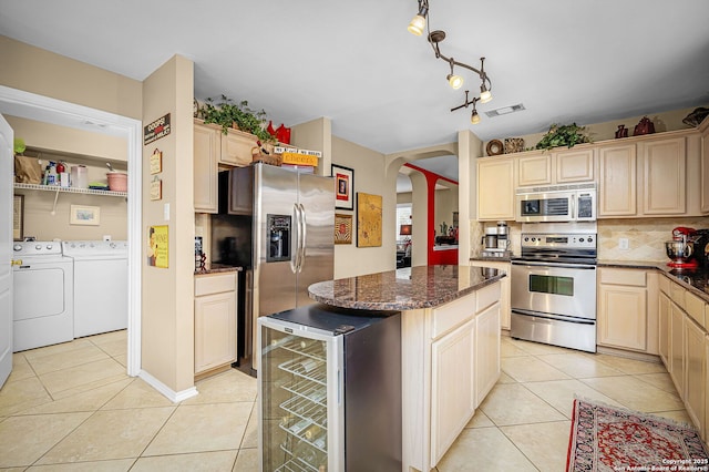 kitchen with light tile patterned floors, appliances with stainless steel finishes, wine cooler, washing machine and clothes dryer, and dark stone counters