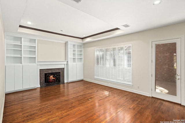 unfurnished living room featuring recessed lighting, wood-type flooring, a raised ceiling, and a fireplace with flush hearth