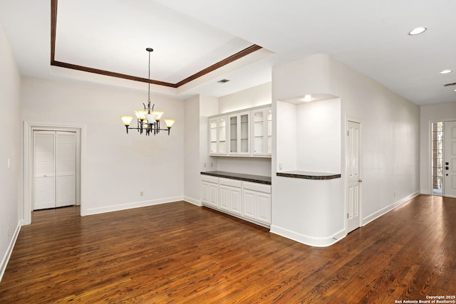 unfurnished room with an inviting chandelier, a raised ceiling, dark wood finished floors, and baseboards