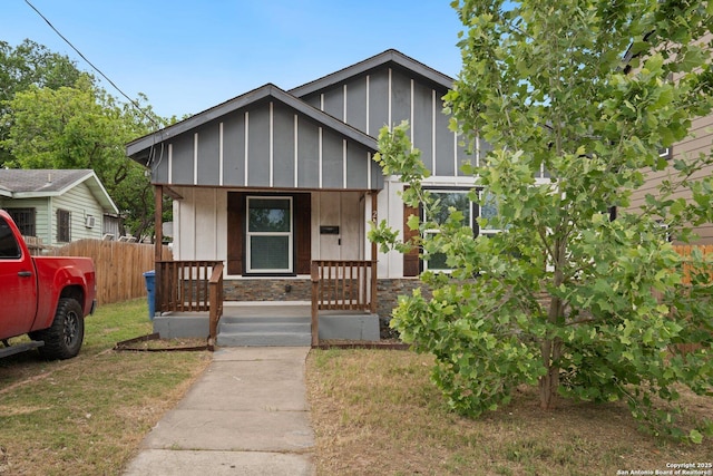 view of front of house with board and batten siding, a porch, stone siding, and fence