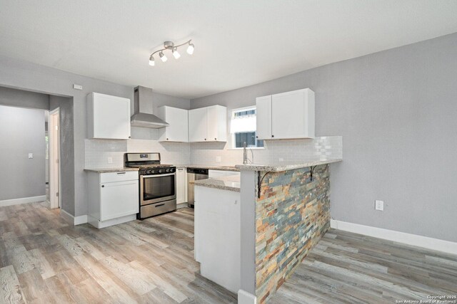 kitchen featuring backsplash, wall chimney exhaust hood, stainless steel appliances, and light wood-style floors