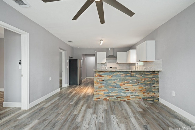 kitchen with wall chimney range hood, ceiling fan, white cabinetry, visible vents, and freestanding refrigerator