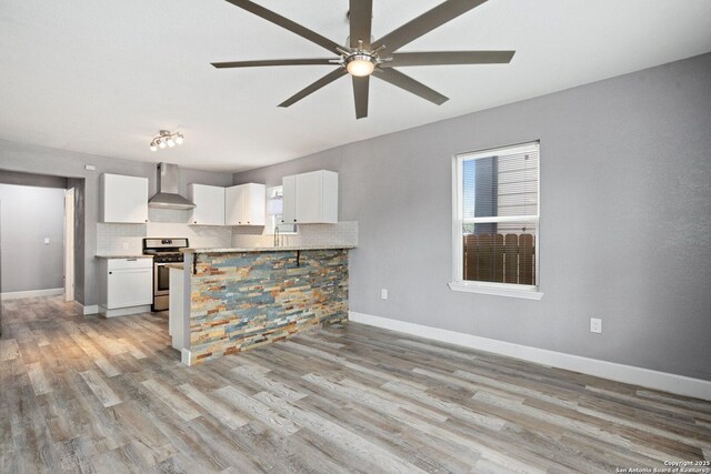 kitchen featuring white cabinets, light wood finished floors, wall chimney exhaust hood, gas range, and ceiling fan