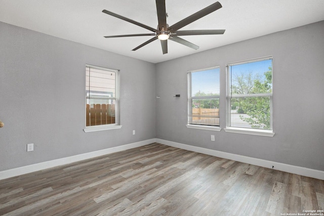 empty room with plenty of natural light, baseboards, wood finished floors, and ceiling fan