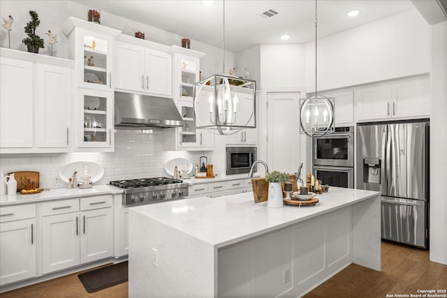 kitchen featuring white cabinetry, appliances with stainless steel finishes, an island with sink, and decorative light fixtures