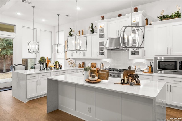 kitchen with hanging light fixtures, white cabinetry, a kitchen island, and stainless steel microwave