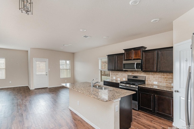 kitchen with appliances with stainless steel finishes, tasteful backsplash, sink, a kitchen island with sink, and dark brown cabinetry