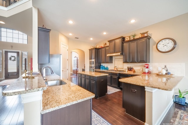 kitchen with dark brown cabinetry, sink, a breakfast bar area, light stone counters, and kitchen peninsula