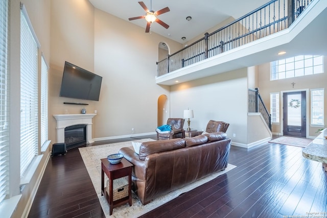 living room with a high ceiling, dark wood-type flooring, and ceiling fan