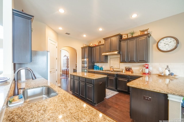 kitchen featuring sink, dark brown cabinets, appliances with stainless steel finishes, a kitchen island, and light stone countertops