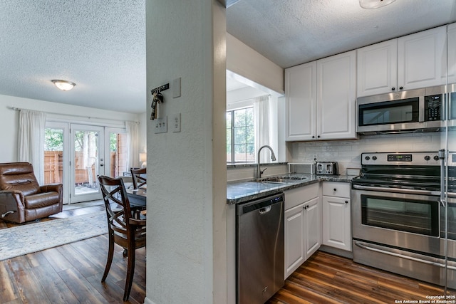 kitchen with sink, appliances with stainless steel finishes, white cabinetry, dark stone countertops, and tasteful backsplash