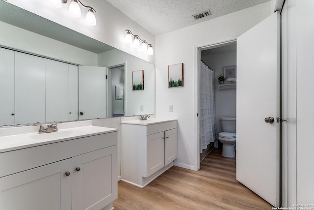 bathroom with hardwood / wood-style flooring, vanity, a textured ceiling, and toilet