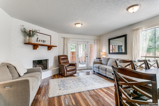 living room featuring a brick fireplace, dark hardwood / wood-style floors, a textured ceiling, and french doors