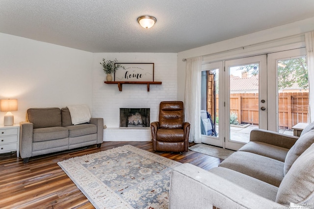 living room featuring a brick fireplace, dark wood-type flooring, french doors, and a textured ceiling