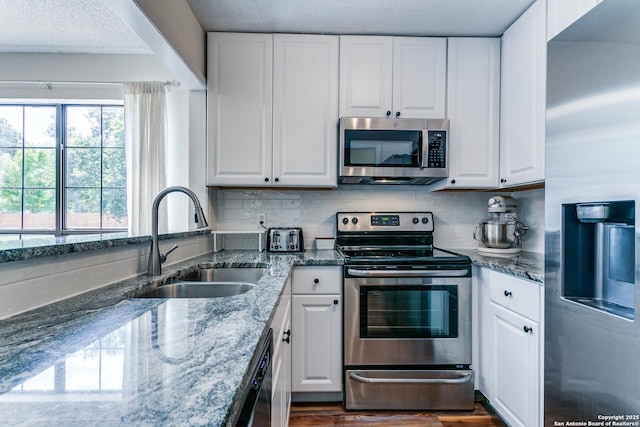 kitchen with sink, appliances with stainless steel finishes, white cabinetry, backsplash, and dark stone countertops