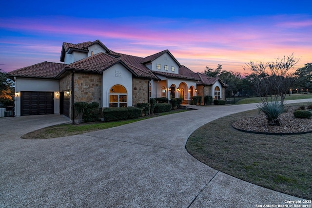 mediterranean / spanish house with stone siding, curved driveway, a tile roof, and stucco siding