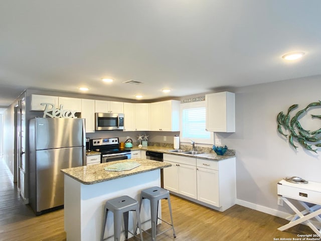 kitchen with a kitchen island, white cabinetry, sink, stainless steel appliances, and light stone countertops