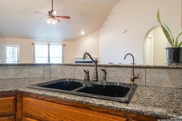 kitchen featuring ceiling fan, lofted ceiling, sink, and dark stone countertops