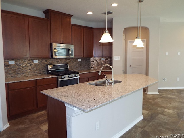 kitchen with appliances with stainless steel finishes, decorative light fixtures, an island with sink, sink, and light stone countertops