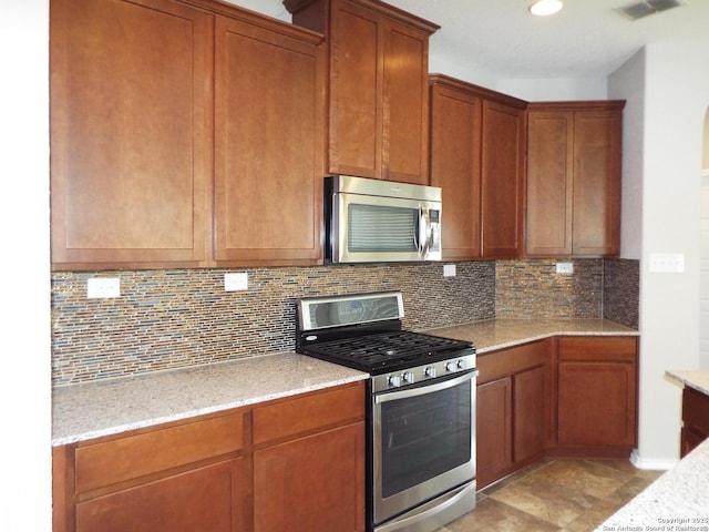 kitchen featuring stainless steel appliances, backsplash, and light stone counters