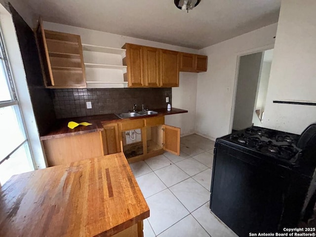 kitchen with butcher block counters, sink, light tile patterned floors, gas range oven, and decorative backsplash