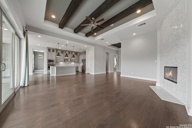 unfurnished living room with a large fireplace, dark hardwood / wood-style flooring, a towering ceiling, ceiling fan, and beam ceiling