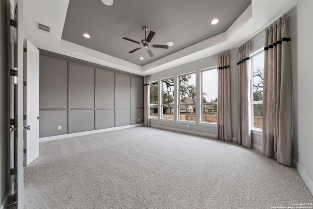 unfurnished room featuring a tray ceiling, light colored carpet, and ceiling fan