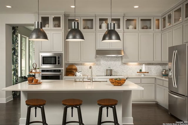 kitchen with pendant lighting, an island with sink, sink, backsplash, and stainless steel appliances